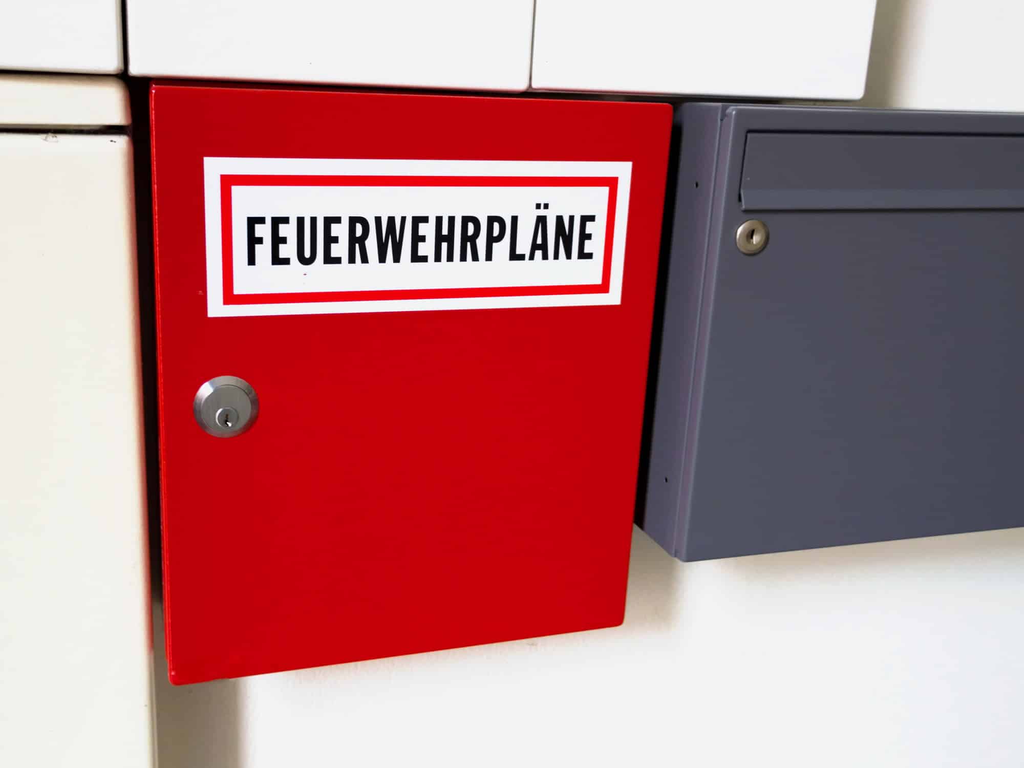 Rotes Feuerwehrplandepot mit der Aufschrift Feuerwehrpläne an einer Wand neben einem Briefkasten
