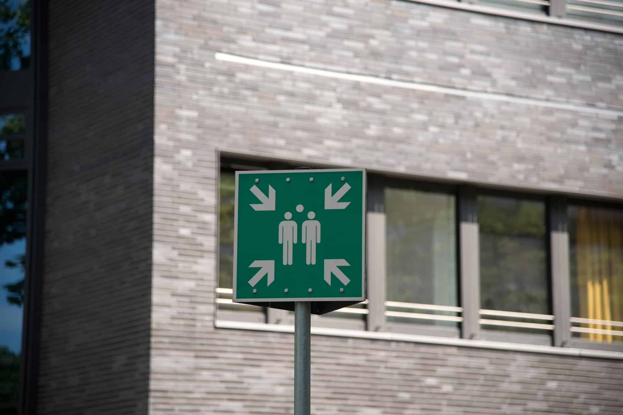 Schild Sammelstelle nach DIN EN ISO 7010 vor einem Bürogebäude